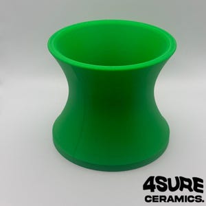 Könnte beinhalten: Eine hellgrüne Keramikvase in Sanduhrform. Die Vase hat eine breite Ober- und Unterseite mit einem schmaleren Mittelteil. Der Text "4SURE CERAMICS" ist unten in Schwarz gedruckt.
