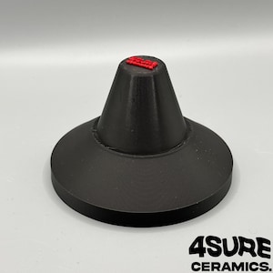 Pode incluir: Um suporte de exibição de cerâmica preta com uma base circular larga e um topo cônico. O topo tem um pequeno texto vermelho. As palavras "4SURE CERAMICS" são impressas em branco na parte inferior.