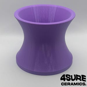 May include: A purple ceramic vase with a unique hourglass shape. The vase has a wide base and top, with a narrower midsection. The bottom right corner of the image has the text "4SURE CERAMICS."