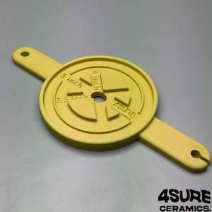 May include: A yellow circular ceramic tool with two extended handles featuring holes at each end. The surface displays embossed text reading 3.5 inch, 4 inch, 5 inch, and 4SURE CERAMICS, with a central hole and raised geometric segments.