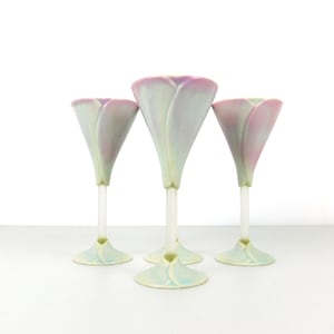 May include: A set of four glass goblets featuring a tulip-shaped bowl with a soft gradient of pastel pink, blue, and green hues. Each goblet has a slender, clear stem and a flared base that mirrors the petal-like design of the bowl top.