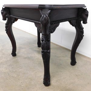 May include: Dark brown antique table with carved horse head details on the corners. The table has ornate, curved legs and a decorative rope-like trim along the apron. The table's dimensions are approximately 30 inches long, 20 inches wide, and 28 inches high.