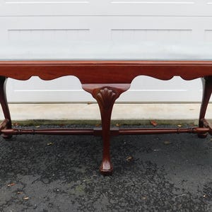 May include: A mahogany-colored bench with a light gray upholstered top. The bench features ornate, curved legs and a decorative apron. The legs are carved with a detailed design. The bench is approximately 60 inches long.