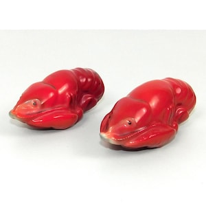 Puede incluir: Dos figuritas de langosta de cerámica roja. Las langostas están en posición enroscada con sus colas metidas debajo de sus cuerpos.