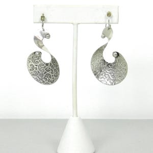 May include: A pair of silver dangle earrings with a swirl design and a textured surface.
