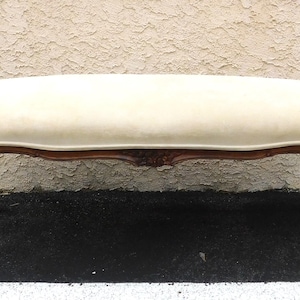 May include: A long bench featuring a cream-colored upholstered seat and a dark brown wooden frame. The base is supported by four curved legs with intricate carved detailing along the apron and the upper sections of the legs.