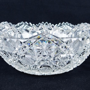 May include: A clear, cut-glass bowl with a scalloped rim. The bowl features intricate geometric patterns, including diamonds and starbursts. The bowl is likely made of lead crystal and is designed for decorative or serving purposes.