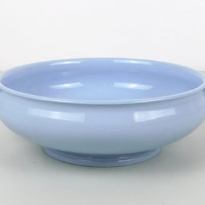 Może przedstawiać: Jasnoniebieska ceramiczna miska do serwowania z dwoma małymi uchwytami po bokach. Miska ma okrągłą podstawę i szeroki, płytki otwór. Miska jest w jednolitym, bladoniebieskim kolorze i wydaje się być glazurowana.