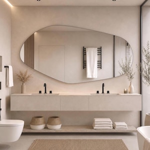 May include: A bathroom vanity featuring a large, irregular, organic-shaped mirror mounted above a long, floating beige cabinet with two sinks, black faucets, and open shelving below containing woven baskets and stacks of white towels.