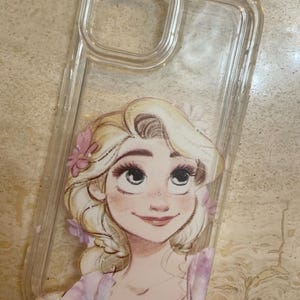 May include: Clear phone case featuring a cartoon illustration of a blonde woman with pink flowers in her hair. The case is made of transparent plastic and has a cutout for the camera and buttons.
