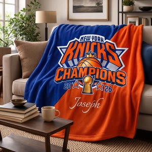 May include: A plush throw blanket featuring a split blue and orange design with the New York Knicks Champions logo, a basketball with a crown, a trophy, the years 2020 and 2026, and the name Joseph printed in white script lettering.