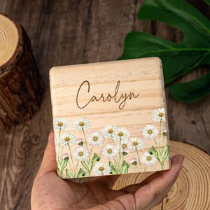 May include: A wooden box with a white daisy floral design and the name "Carolyn" engraved on the front.
