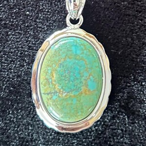 May include: A silver chain necklace with a silver oval pendant featuring a green and gold turquoise stone.