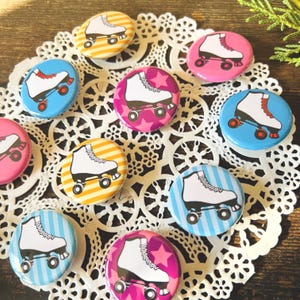 May include: A collection of colorful roller skate pinback buttons. Each button features a white roller skate design on a background of stripes, stars, or solid colors, including pink, blue, and yellow. The buttons are arranged on a white lace doily.