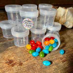 May include: A group of clear plastic jars with lids, some filled with colorful jelly beans. The jars are labeled with the text "#4305 Deco Jars.com".