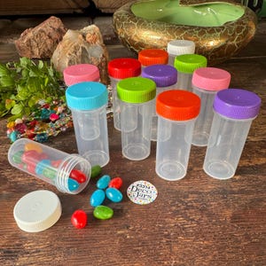 May include: Clear plastic jars with colorful lids in various colors, including red, green, purple, and pink. One jar is open, spilling out colorful candies. A small sticker with the text "#3314 Deco Jars .com" is also visible.