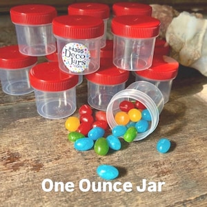May include: A group of clear plastic jars with red lids, some filled with colorful jelly beans. The jars are labeled "#4305 Deco Jars.com". The text "One Ounce Jar" is written below the jars.
