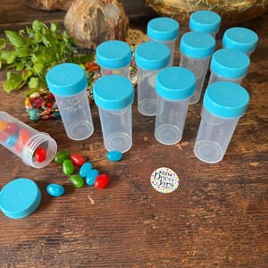 May include: Clear plastic jars with turquoise lids are arranged on a wooden surface. Some jars are upright, while others are open, spilling colorful jelly beans. A logo that says "Deco Jars" is visible.