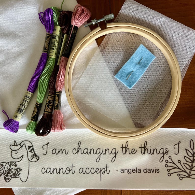 May include: Embroidery kit featuring a wooden hoop, fabric, needles, and colourful embroidery floss. The kit includes fabric printed with the quote "I am changing the things I cannot accept - angela davis".