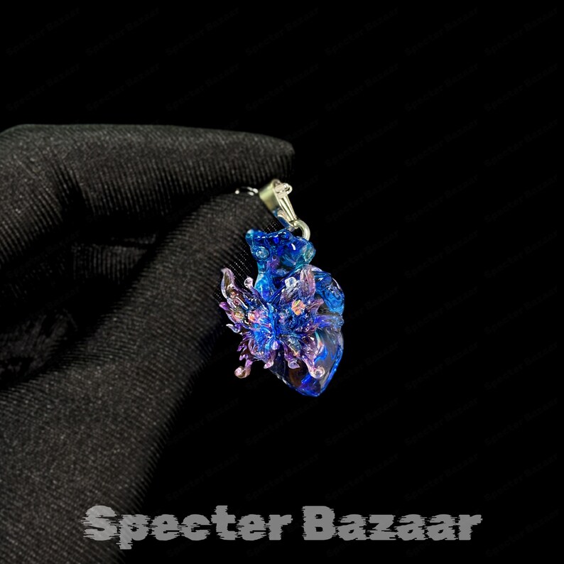 May include: A blue and purple pendant with a butterfly design. The pendant is made of a translucent material and has a silver-colored bail. The text "Specter Bazaar" is at the bottom of the image.