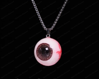 May include: A pendant necklace with a realistic eyeball charm. The charm is pale pink with a dark brown iris and red veins, suspended from a silver-coloured chain. The text "Specter Bazaar" is at the bottom.