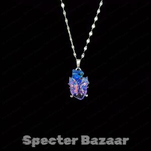 May include: A silver necklace with a pendant featuring a blue and purple design. The pendant has a butterfly-like shape with intricate details. The necklace is displayed against a black background. The text "Specter Bazaar" is at the bottom.