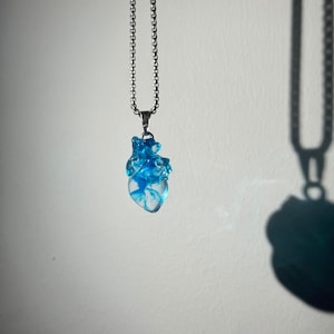 May include: A silver chain necklace with a blue resin anatomical heart pendant.