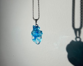 May include: A silver chain necklace with a blue resin anatomical heart pendant.