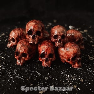 May include: A collection of small, reddish-brown skull figurines with intricate detailing. The skulls are arranged in a pile, creating a striking visual. The background is dark, and the text "Specter Bazaar" is visible at the bottom.
