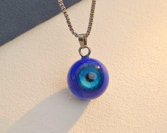 May include: A silver chain necklace with a blue glass eye pendant. The eye is surrounded by a blue circle and has a white pupil.