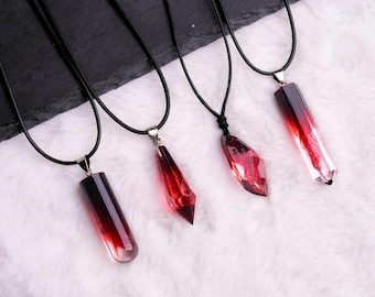 May include: Four necklaces with pendants in shades of red and clear. The pendants are various shapes, including a crystal and a rectangular prism. Each pendant hangs from a black cord. The text "Specter Bazaar" is at the bottom.