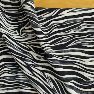 May include: Black and white zebra print fabric with a soft, flowing texture. The fabric has a subtle watercolor effect, giving it a unique and stylish look.