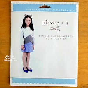 Puede incluir: Un sobre de patrón de costura Oliver + S para una chaqueta y falda Double Dutch. El empaque presenta una foto de un niño usando la chaqueta y la falda, con texto que enumera las tallas de 6-12 M a 12 y el logo de My Little Fabric Shop.