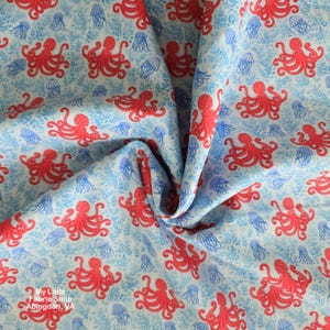 May include: Light blue fabric with a repeating pattern of red octopuses and blue jellyfish. The fabric also features a subtle design of small, light blue plant-like shapes. The fabric is from My Little Fabric Shop, Abingdon, VA.
