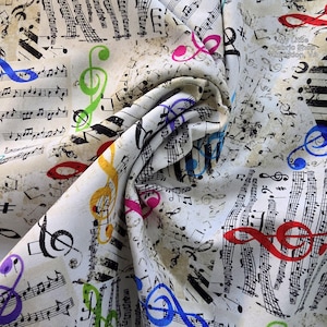 Puede incluir: Tela blanquecina con temática musical. La tela está cubierta de notas musicales, claves de sol y otros símbolos musicales en negro, con claves de sol coloridas en azul, verde, amarillo, rosa y rojo. La tela está doblada, mostrando la textura.