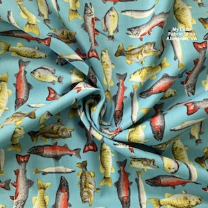 May include: Light blue fabric with a repeating pattern of various fish in shades of yellow, red, and gray. The fabric has a slight texture and a visible fold. The text "My Little Fabric Shop Abingdon, VA" is visible in the upper right corner.