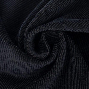 May include: Close-up of a swatch of dark navy blue corduroy fabric. The fabric is folded and draped, showing the texture of the ribbed material. The color is a deep, solid shade of blue.