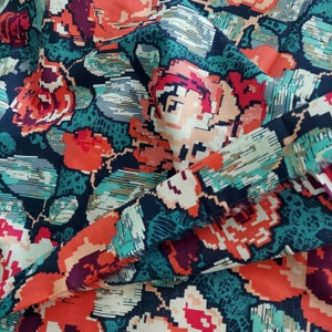 May include: Close-up of a fabric with a floral pattern. The design features pixelated flowers in shades of red, orange, and peach, set against a dark teal and navy blue background. The fabric is folded, showing the texture and detail of the print.