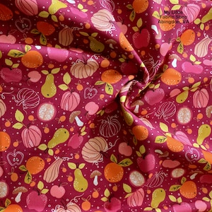 Puede incluir: Primer plano de una tela con fondo burdeos y un patrón repetido de frutas y verduras. El diseño incluye calabazas, manzanas, peras, naranjas y champiñones en tonos rosa, naranja y amarillo. El texto "My Little Fabric Shop Abingdon, VA" es visible.