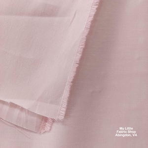 Peut inclure: Gros plan sur un tissu rose pâle avec un bord brut. Le tissu est lisse et présente une texture subtile. Le texte "My Little Fabric Shop Abingdon, VA" est visible dans le coin inférieur droit.