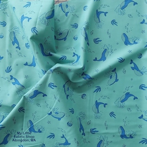 May include: Aqua fabric featuring a repeating pattern of blue whales, sea plants, and fish. The fabric has a soft, slightly wrinkled appearance. The text "My Little Fabric Shop Abingdon, VA" is visible in the lower left corner.