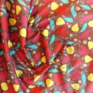 Puede incluir: Tela marrón con un patrón repetido de hojas de otoño y bellotas en tonos rojos, amarillos y turquesas. La tela tiene un ligero brillo y es adecuada para diversos proyectos de manualidades.