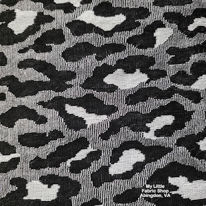 May include: A woven fabric featuring a repeating black and white leopard print pattern. The textile displays a textured surface with high contrast between the dark spots and the lighter background. Text in the corner reads My Little Fabric Shop Abingdon, VA.