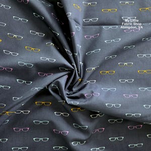 May include: A dark gray fabric featuring a repeating pattern of eyeglasses in yellow, pink, and white. The text "My Little Fabric Shop Abingdon, VA" is printed in white in the upper right corner of the fabric, which is gathered in the center.