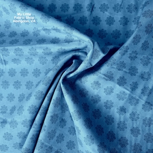 May include: Close-up of blue fabric with a repeating floral pattern. The fabric is slightly wrinkled, creating shadows and depth. The text "My Little Fabric Shop Abingdon, VA" is visible in the upper left corner. The fabric appears to be cotton or a similar material.