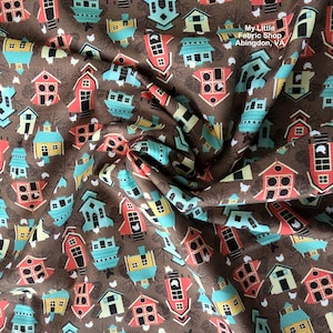 May include: Brown fabric with a repeating pattern of colorful stylized houses in red, teal, yellow, and white. The fabric has a slightly wrinkled texture. The text "My Little Fabric Shop Abingdon, VA" is visible.