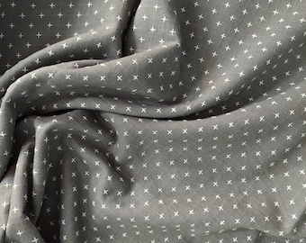 May include: Close-up of a gray fabric with a repeating pattern of small white crosses. The fabric is draped, creating soft folds and shadows. The crosses are evenly spaced across the material.