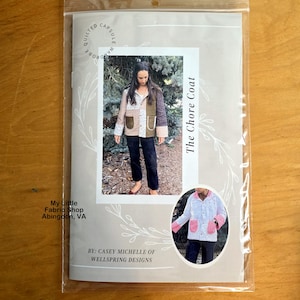 May include: A pattern for "The Chore Coat" is displayed in a clear plastic sleeve. The pattern features a photo of a patchwork jacket with brown, green, and white fabric. The text "My Little Fabric Shop Abingdon, VA" is visible.