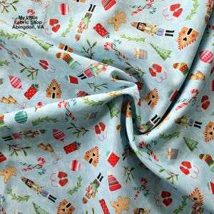 Puede incluir: Tela azul claro con un estampado navideño repetido. El diseño incluye hombres de jengibre, cascanueces, bastones de caramelo, árboles de Navidad, mitones y cajas de regalo. El texto "My Little Fabric Shop Abingdon, VA" es visible.