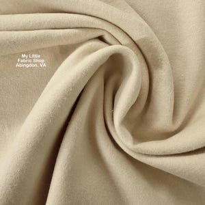 Op de afbeelding: Close-up van een beige stof met zachte plooien en een getextureerd oppervlak. De stof lijkt een materiaal van gemiddeld gewicht te zijn, geschikt voor diverse naaiprojecten. De tekst "My Little Fabric Shop Abingdon, VA" is zichtbaar.